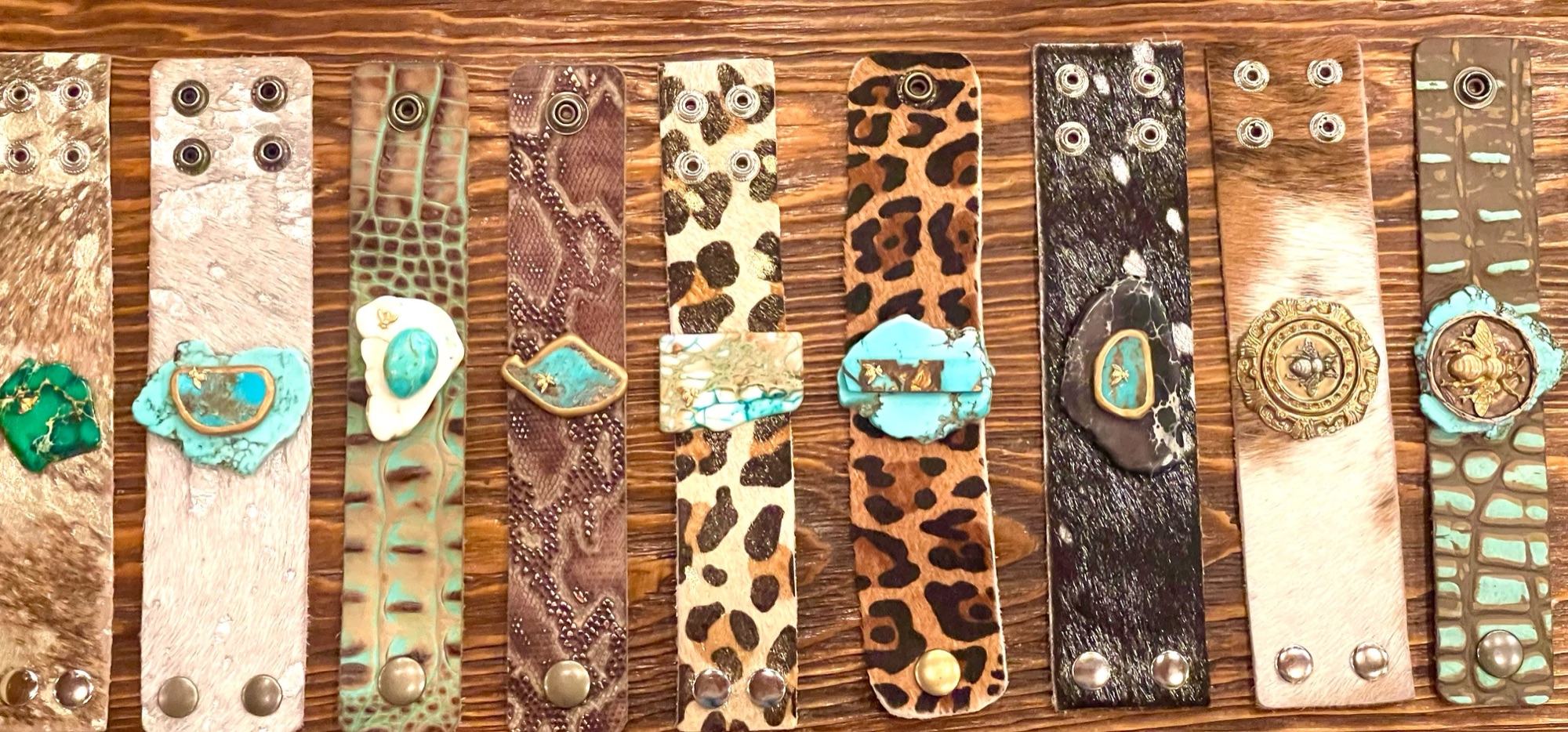 Ten leather cuffs in animal prints and crocodile with turquoise stones, lined up on wood