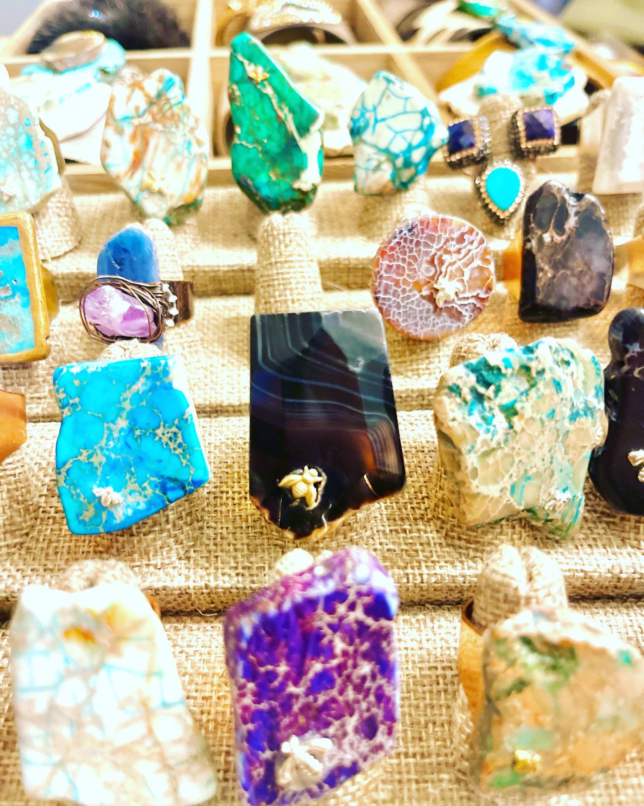 Rows of large stone rings in blue, purple, black, white and green on burlap